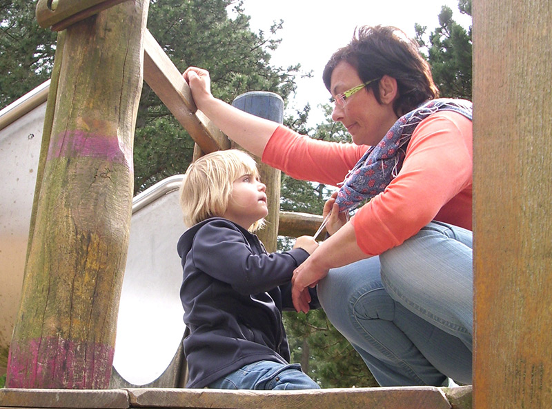 Auf dem Foto sehen Sie Kinder und Erzieherinnen in der Runde sitzen und eine Handbewegung der Gebärdensprache ausführen.