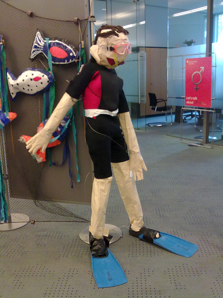 Aus Papier gebastelte bunte Fische und ein lebensgrosser Taucher mit Taucherbrille und Flossen sind auf diesem Bild zu sehen.